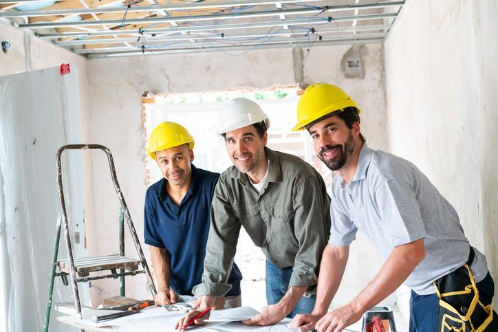 Three smiling contractors reviewing project drawings during acoustic installation